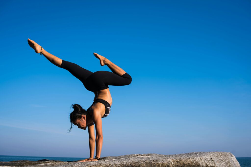 pexels-photo-317155-317155 A woman performing a yoga handstand on a rock by the sea under a clear blue sky.